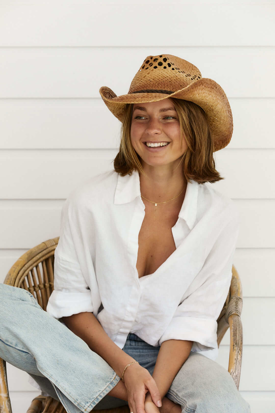 Woman sitting in chair smiling wearing straw Western vented crown hat with vegan leather braided band