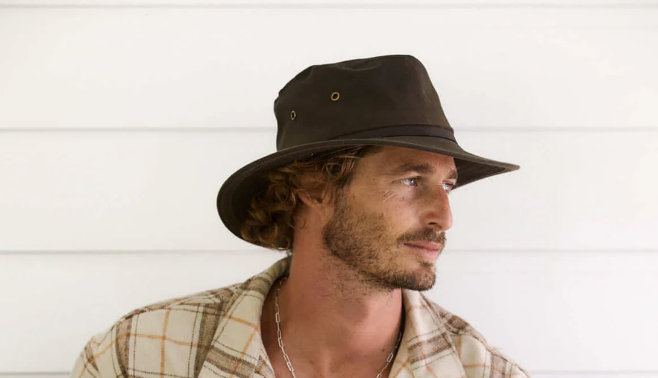 man wearing a brown hiking hat and a flannel looks to the right.