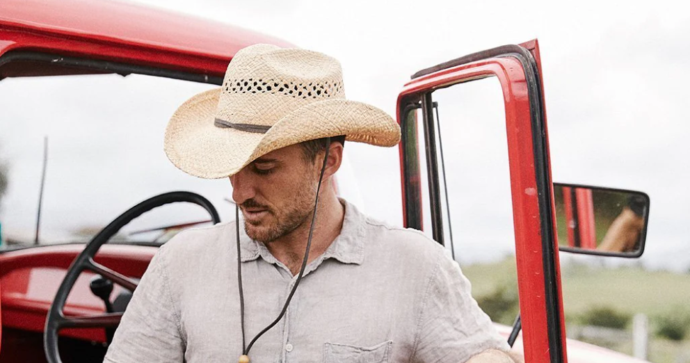 A man wearing a straw cowboy hat steps out of a red truck.