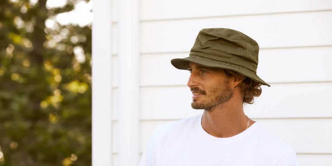 a man wearing an olive green bucket hat looks to the side.