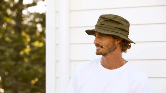 Man wearing an olive green bucket hat and white T-Shirt looks into the distance.