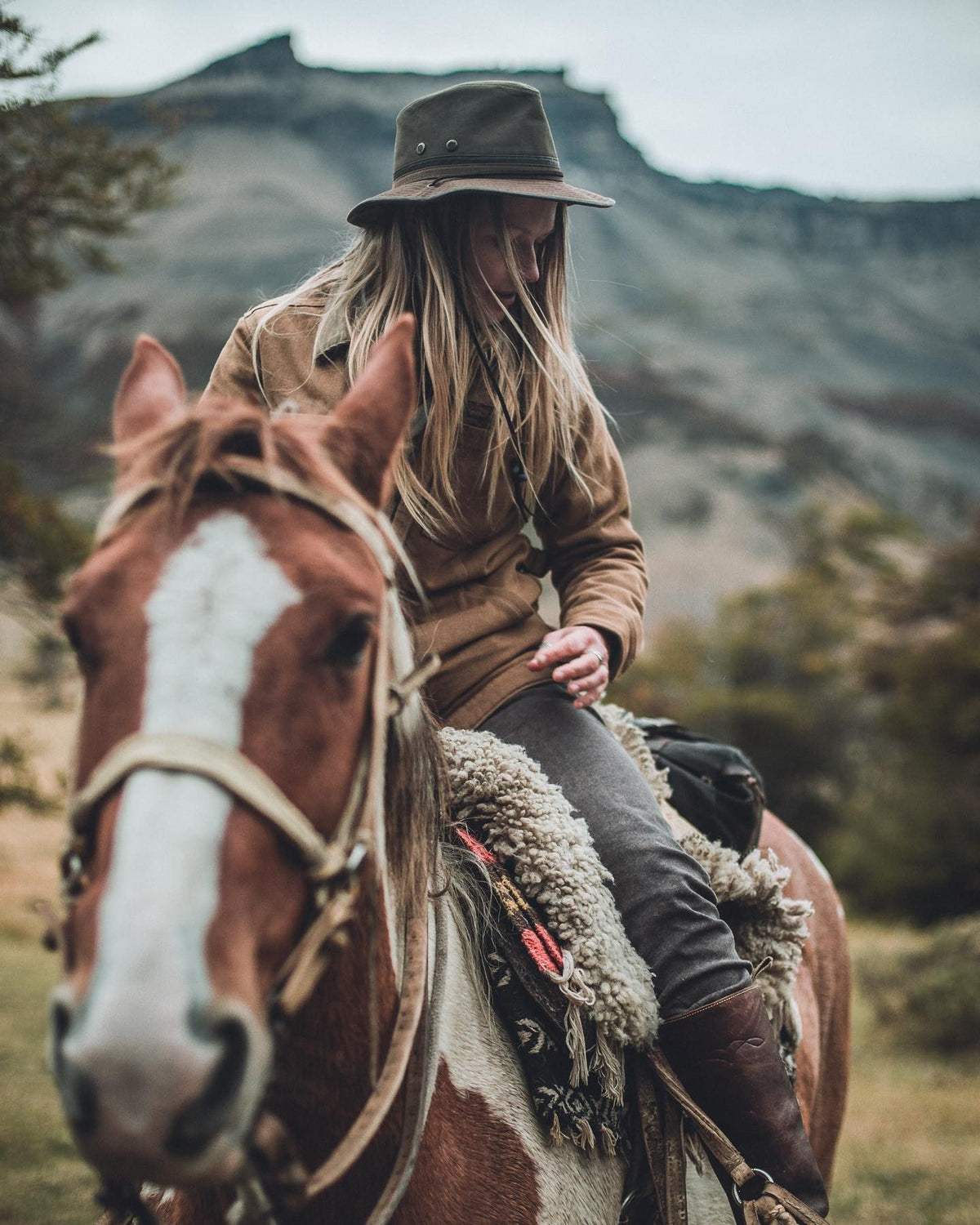 Woman riding a horse on a mountain trail, wearing the Mountain Trail waxed cotton outback hat by Conner Hats