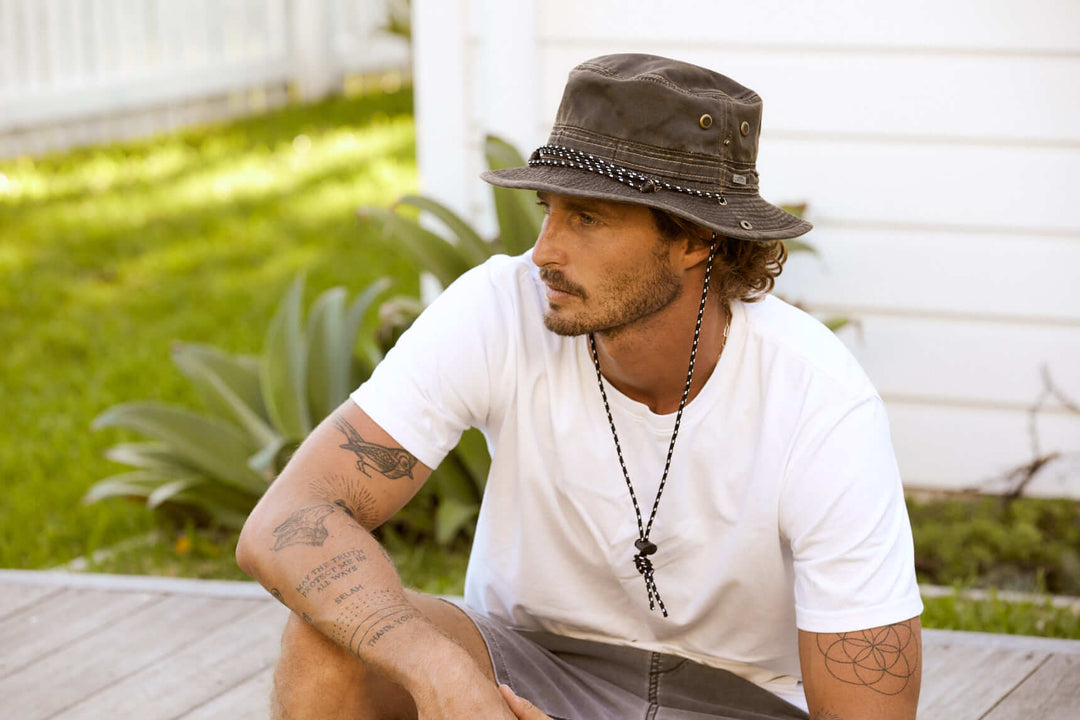 Mad sitting outside wearing Conner Hats Mountain Ventilated Packer cloth Bucket hat with brass colored mesh eyelets for ventilation and chin cord and snap up side