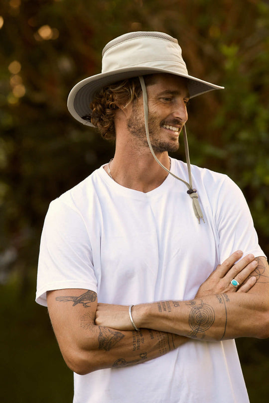 Man outside wearing Conner hats Khaki colored recycled cloth boating sailing hat Hat that floats and has a sun protective ventilation system and secure chin cord for hands free work