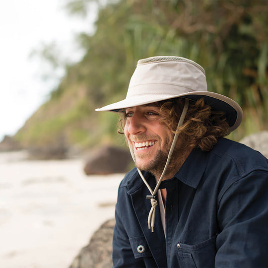 Man on the beach wearing Sand colored recycled cloth boating sailing hat Hat that floats and has a sun protective ventilation system and secure chin cord for hands free work