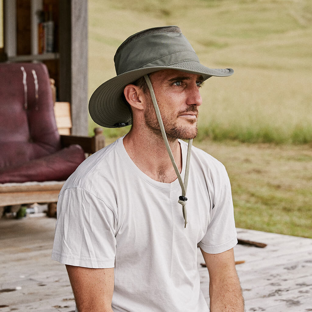 Man on deck wearing Olive colored recycled cloth boating sailing hat Hat that floats and has a sun protective ventilation system and secure chin cord for hands free work