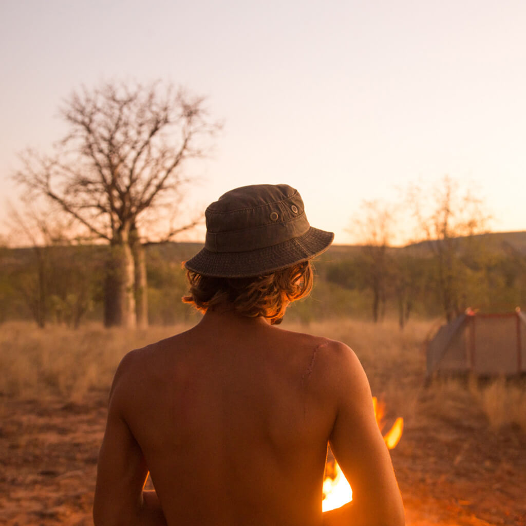 Man at a campfire in Australian Outback wearing waterproof cloth bucket Hat with brass colored mesh eyelets and Conner Hat emblem
