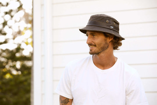 Man smiling standing outside wearing waterproof cloth bucket Hat with brass colored mesh eyelets and Conner Hat emblem