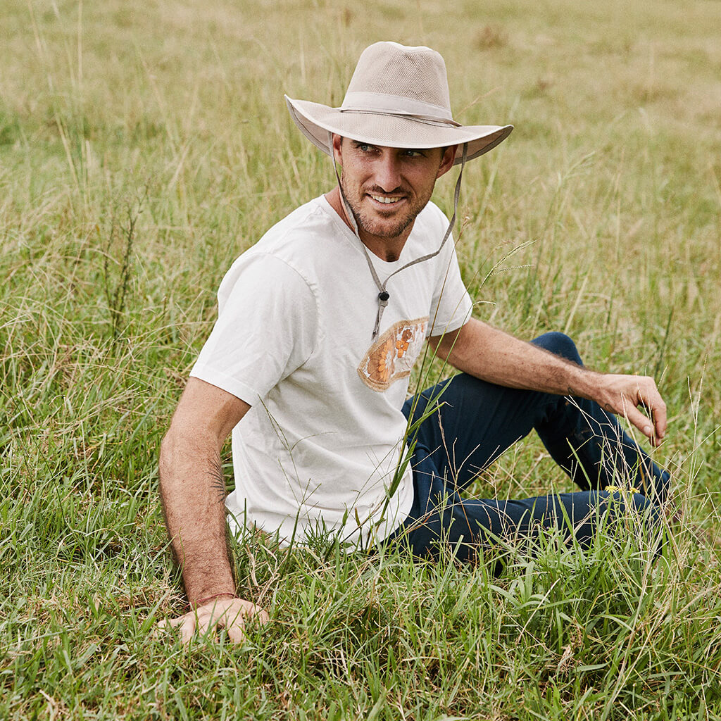 Man outside in grass smiling wearing lightweight cloth hiking sun protection hat with chin cord in outback style