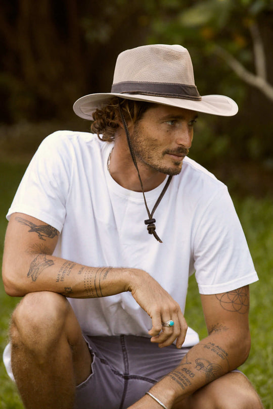 Man outside wearing recycled cloth hiking hat in sand color with Brown band and chin cord also features a cool mech crown