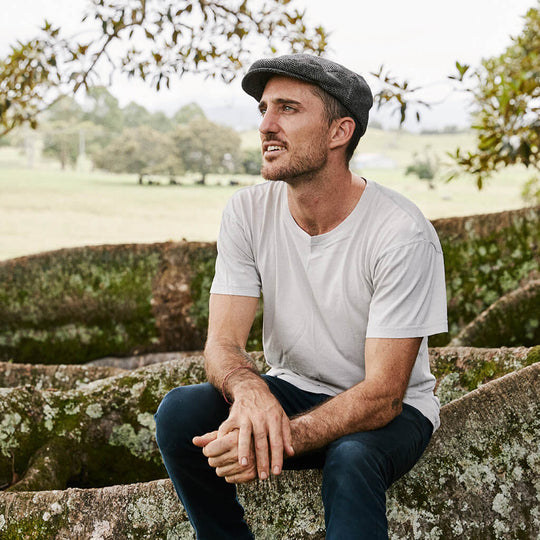 Man sitting in Newsboy flat Cap outdoors under a tree