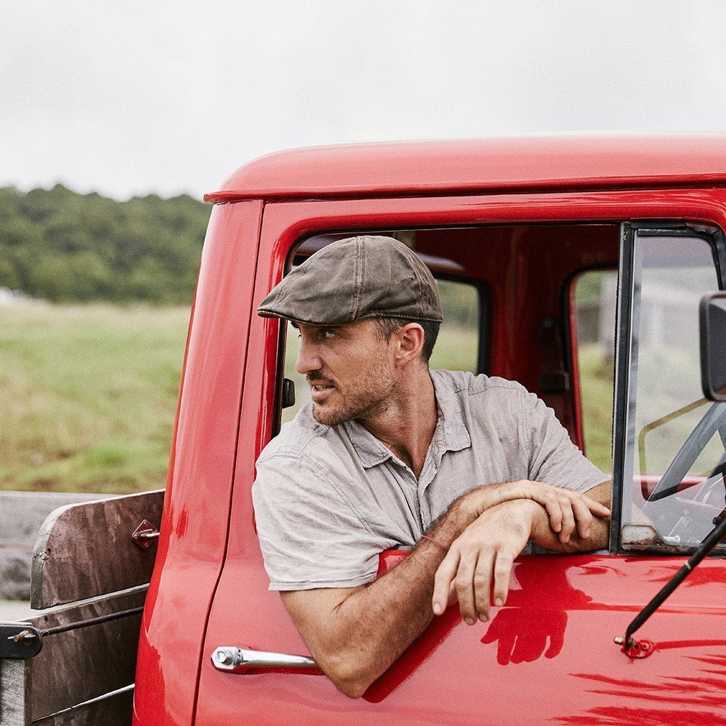 Man in red farm truck wearing Brown cloth newsboy cap that looks like leather