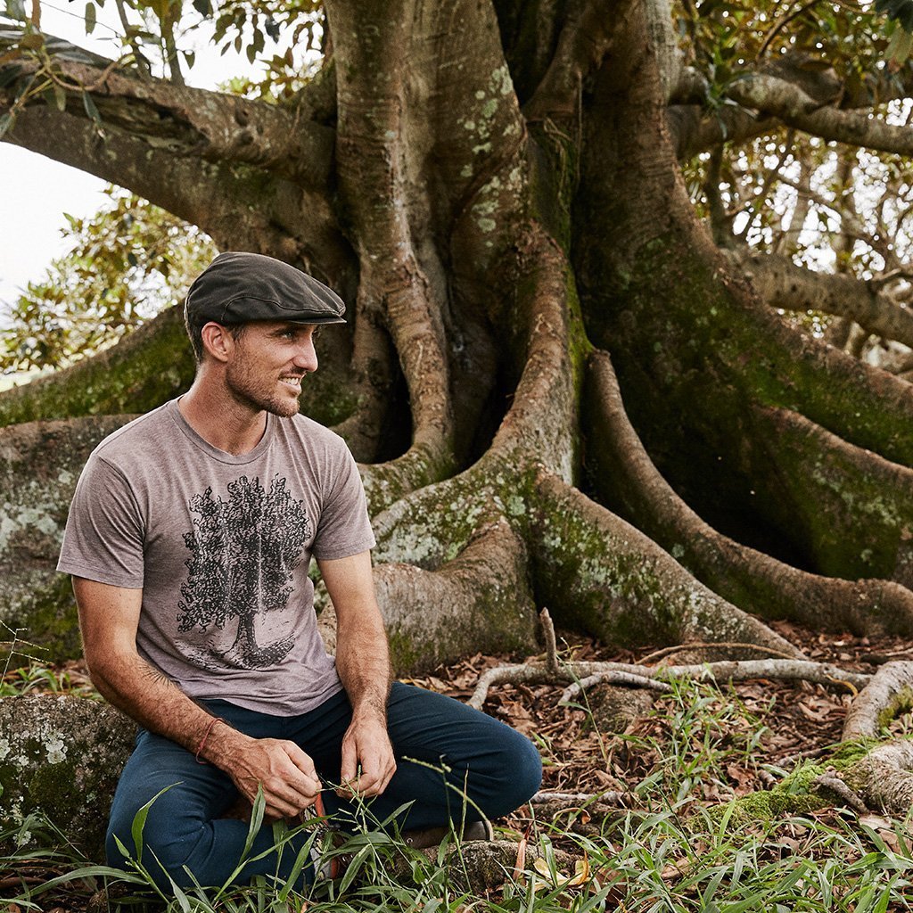 Man sitting outside under a fig tree wearing waterproof cloth newsboy flat cap in color Brown