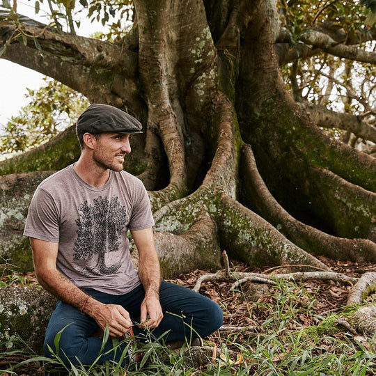 Man sitting outside under a fig tree wearing waterproof cloth newsboy flat cap in color Brown