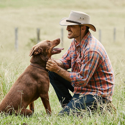 Man patting a brown dog on a farm in Aussie style Outback Beige canvas hat with a mesh crown showing the curve of the brim and contrasting band and chin cord