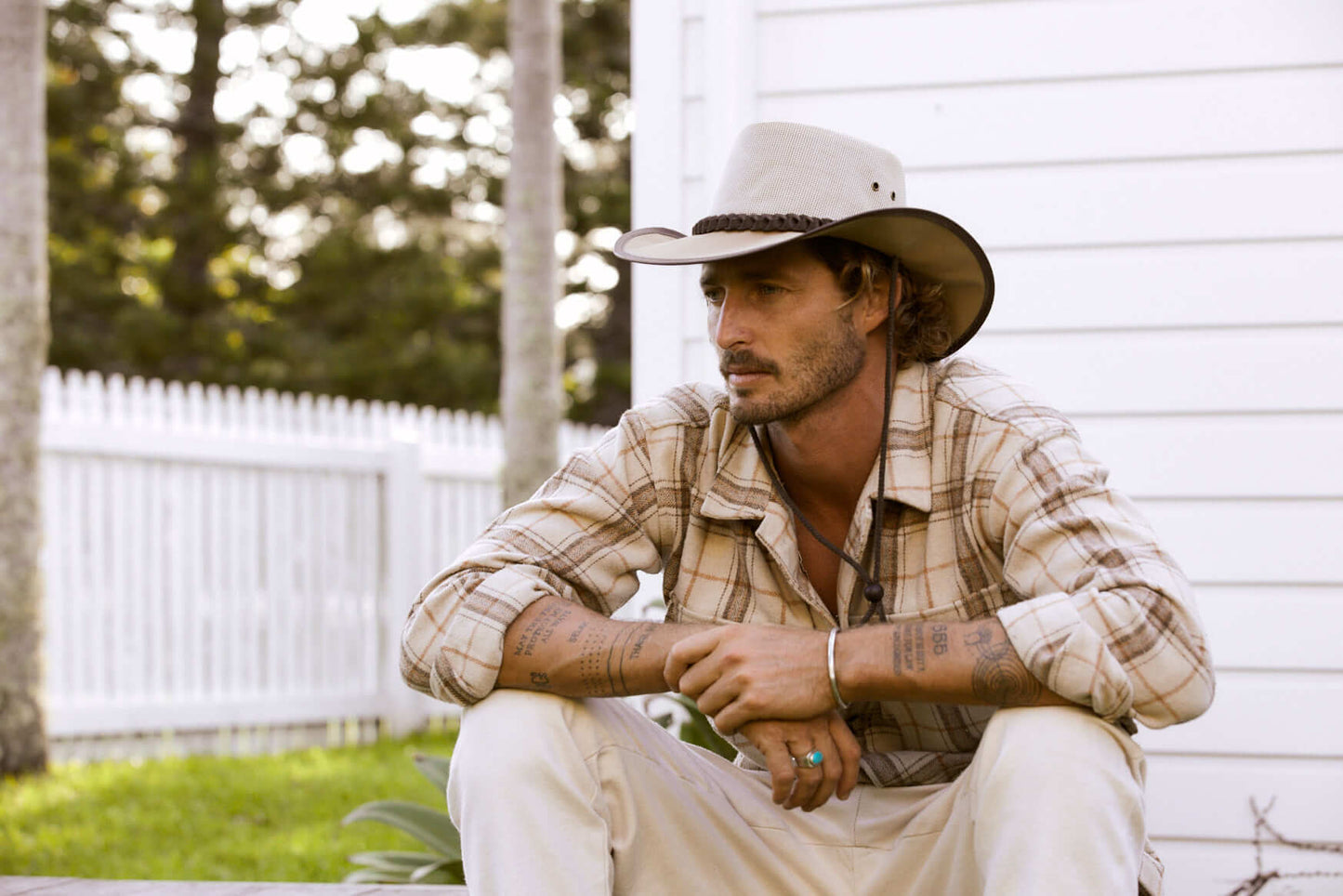 Man sitting in Aussie style Outback Beige canvas hat with a mesh crown including a Brown braided hat band and chin cord