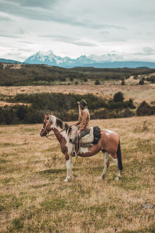 Woman on horseback in Patagonia wearing Australian outback oilskin cotton hat with leather chin cord and brass colored mesh eyelets