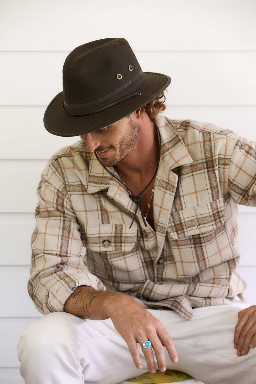 Man outside wearing Australian outback oilskin cotton hat with leather chin cord and brass colored mesh eyelets