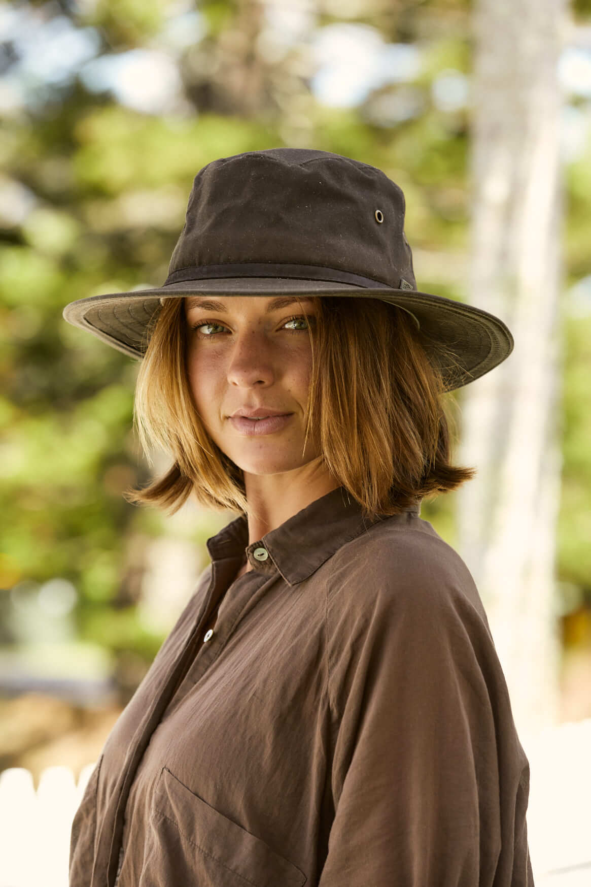 Woman outdoors wearing Brown oilcloth Hat with brass colored eyelets and wide sun protection brim