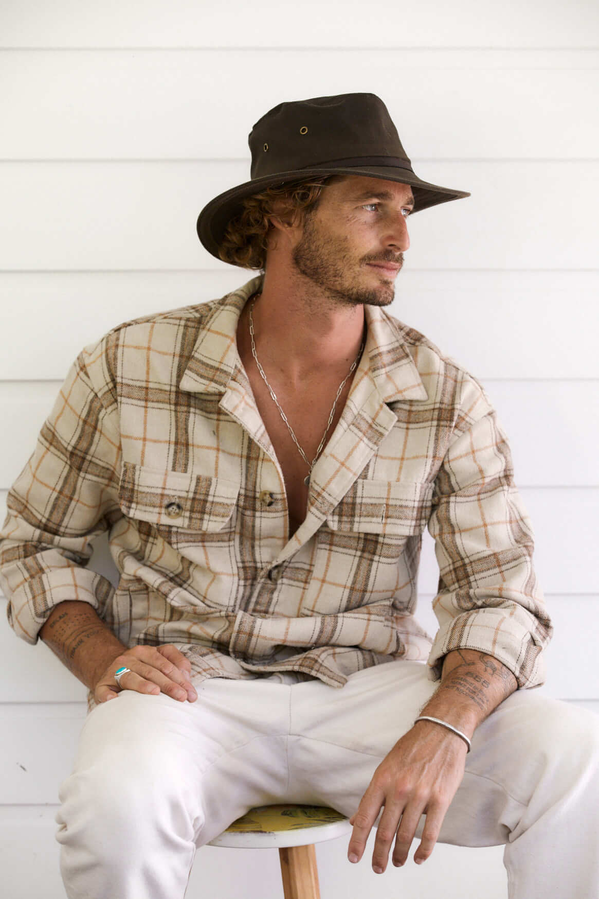 Man looking relaxed sitting outside in Brown oilcloth Hat with brass colored eyelets and wide sun protection brim