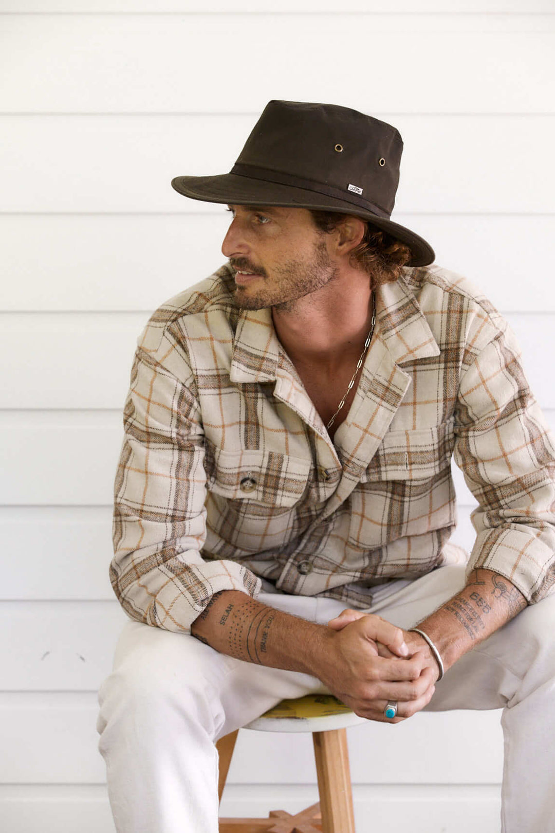 Man sitting outside in Brown oilcloth Hat with brass colored eyelets and wide sun protection brim