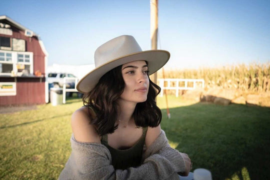 Woman with dark hair out side of a barn wearing boho rancher style wide brim hat in color Putty