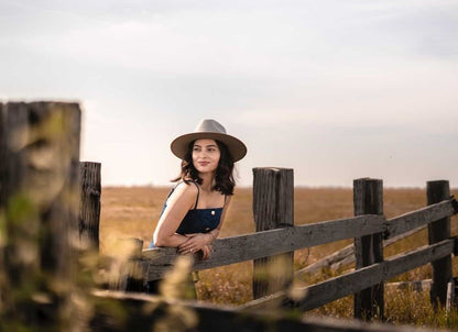 Woman standing along a fenceline boho rancher style wide brim hat in color Putty