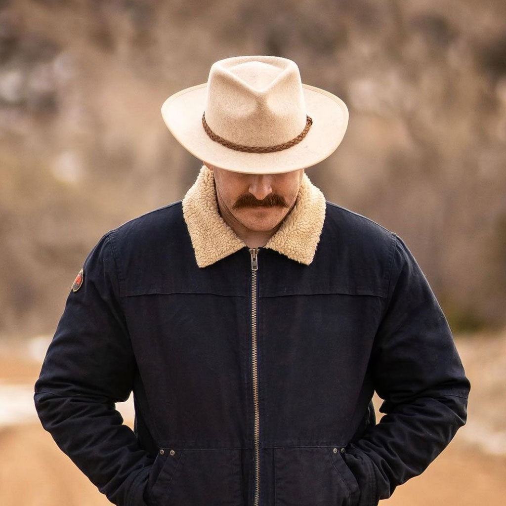 Front view of man in blue jacket with wool collar wearing outback style hat with stiff brim and bound edge with a braided vegan band