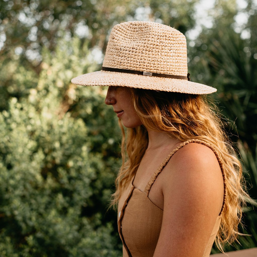 Woman on walking trail wearing hand crocheted raffia straw sun hat with brown faux leather band