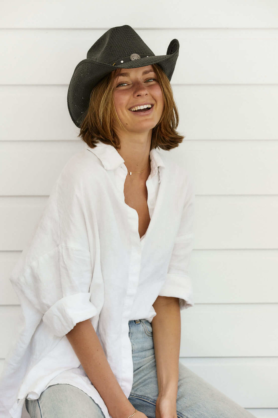 Woman sitting wearing Conner Hats western straw hat in color Black with silver conch and faux leather band