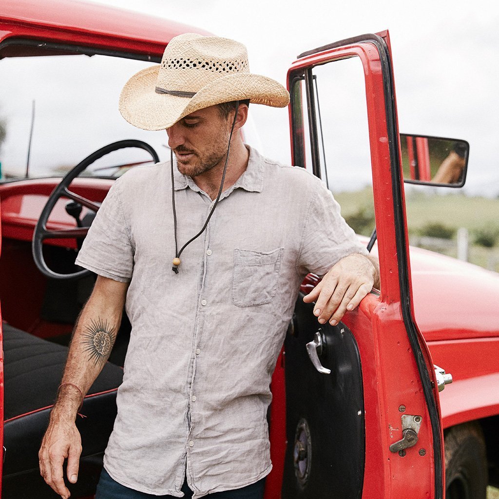 Man standing next to red truck in straw western hat cattleman crown with vented crown and leather chin cord