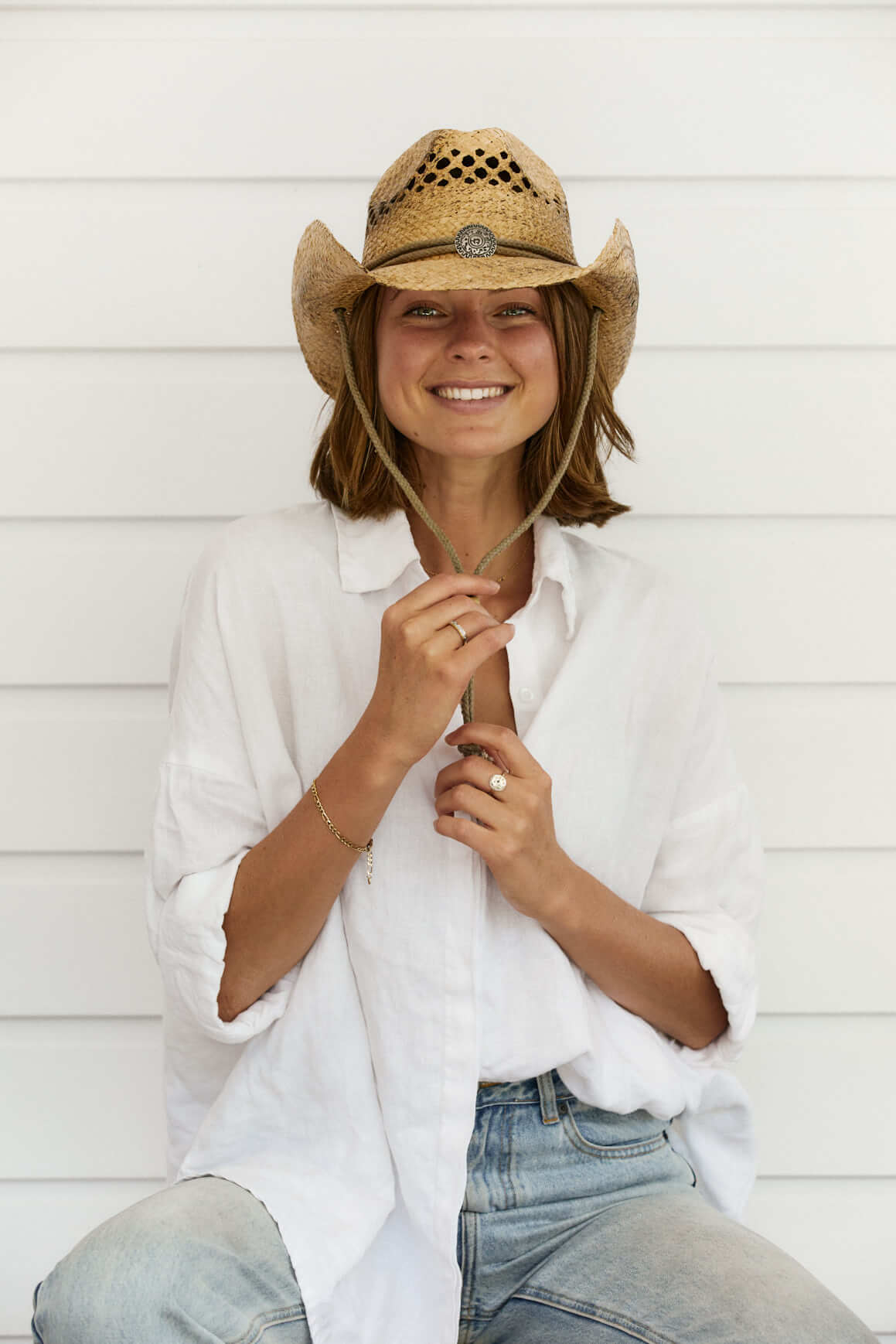 Woman smiling in hand braided raffia straw western hat with vented crown in Coffee color holding chin cord