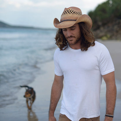 Man walking on beach with dog wearing straw Western vented crown hat with vegan leather braided band