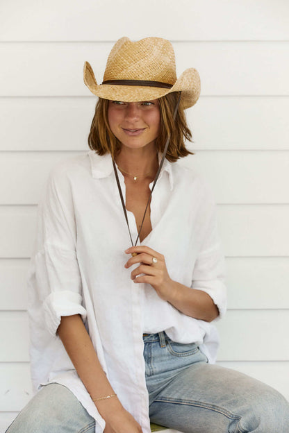 Woman sitting down smiling wearing the Conner Hats Original western raffia hand braided straw western hat with a leather chin cord