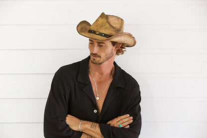 Man outside wearing Coffee stained straw western hat with shapeable brim and brass colored concho on black vegan band