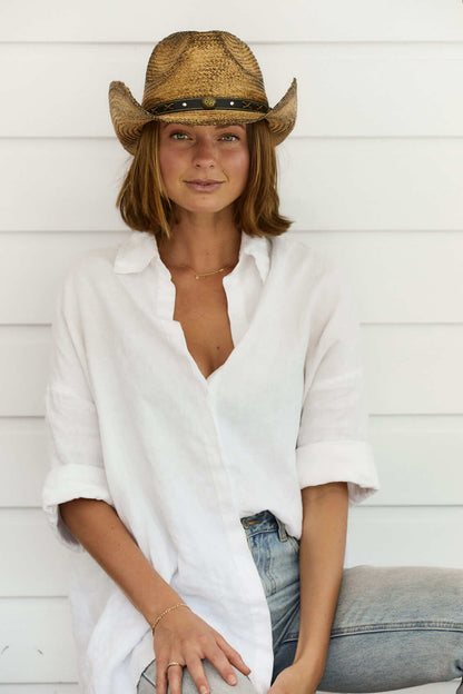 Woman sitting in White shirt wearing Conner Hats Coffee stained straw western hat with shapeable brim and brass colored concho on black vegan band