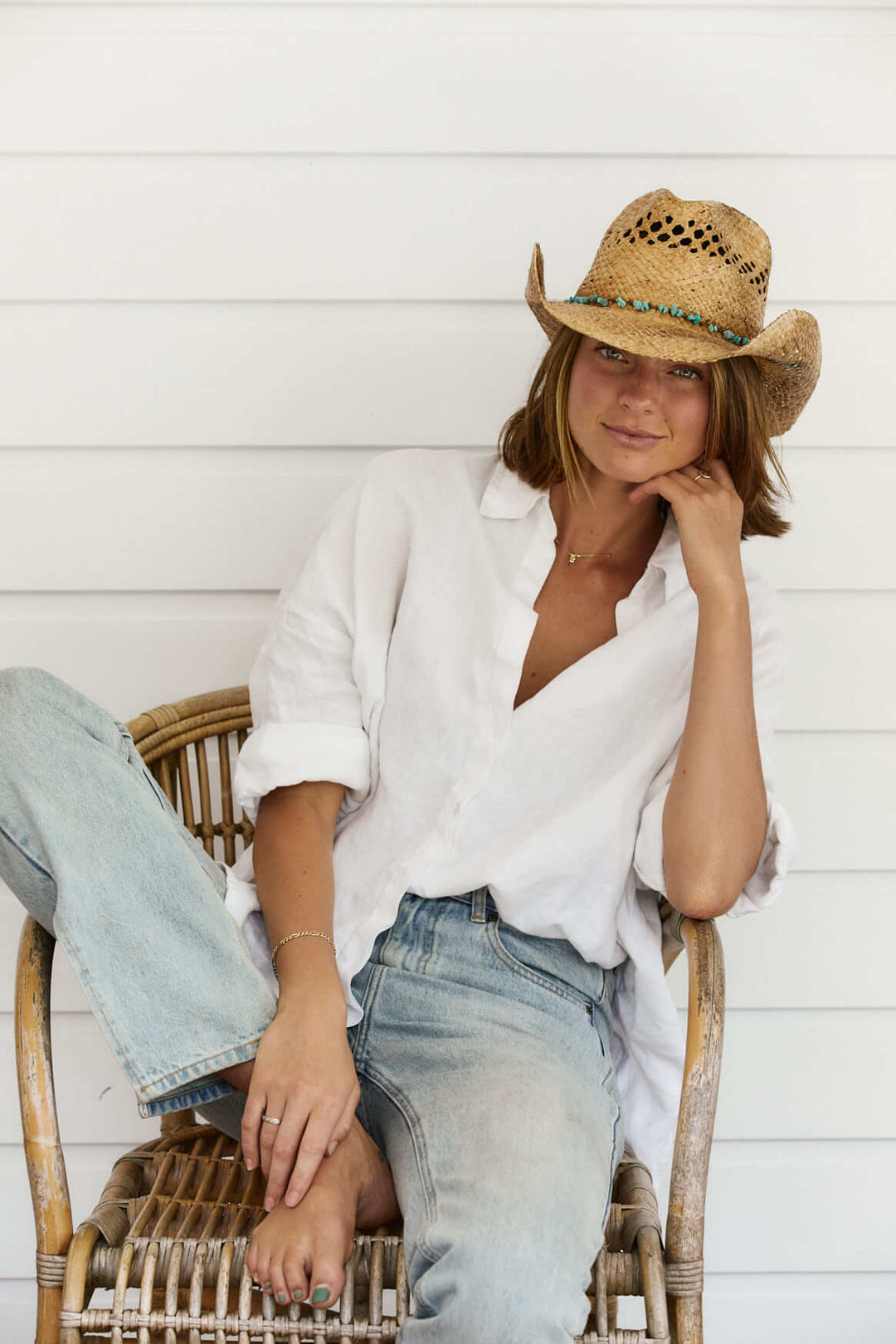 Woman lounging on a chair wearing her Conner Hats Durango raffia straw western hat with Turquoise colored stones and shapeable brim with vented crown