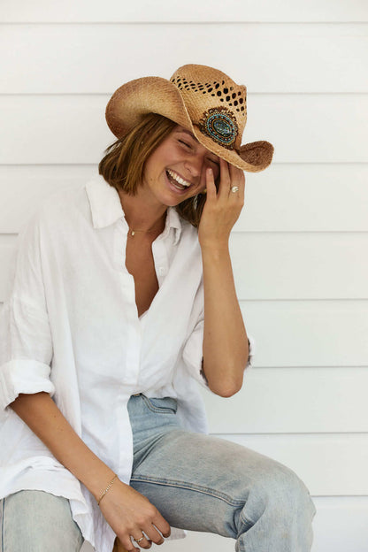 Woman laughing wearing blue jeans and  Conner hats raffia straw western women's hat with vented crown and beautiful beaded feather concho