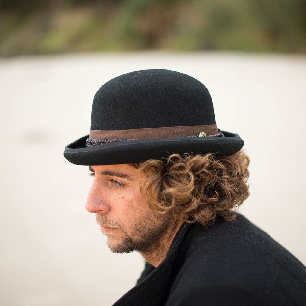 Man in the great outdoors wearing wool bowler/derby hat in color Black with a braided Black and Brown band and brass colored emblem