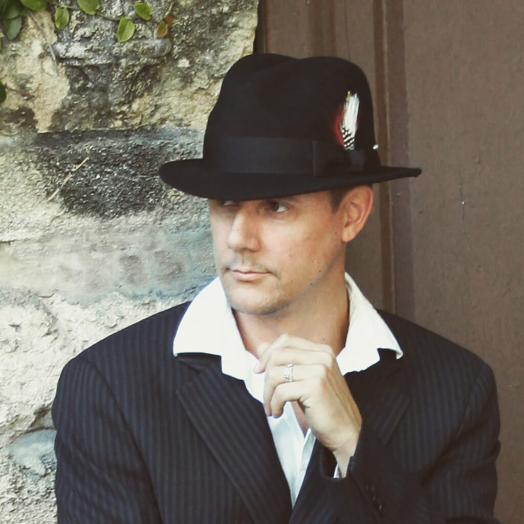 Man standing outside in a suit in Conner hats Detroit fedora wool hat with grosgrain bow band and feather accent also featuring a snap up brim