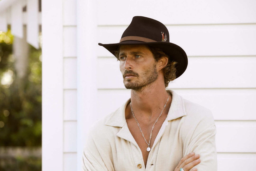 Man outside in cruelty free crushable wool outback style hat in color Black with pinched crown and faux leather Brown hat band with stitching and a feather