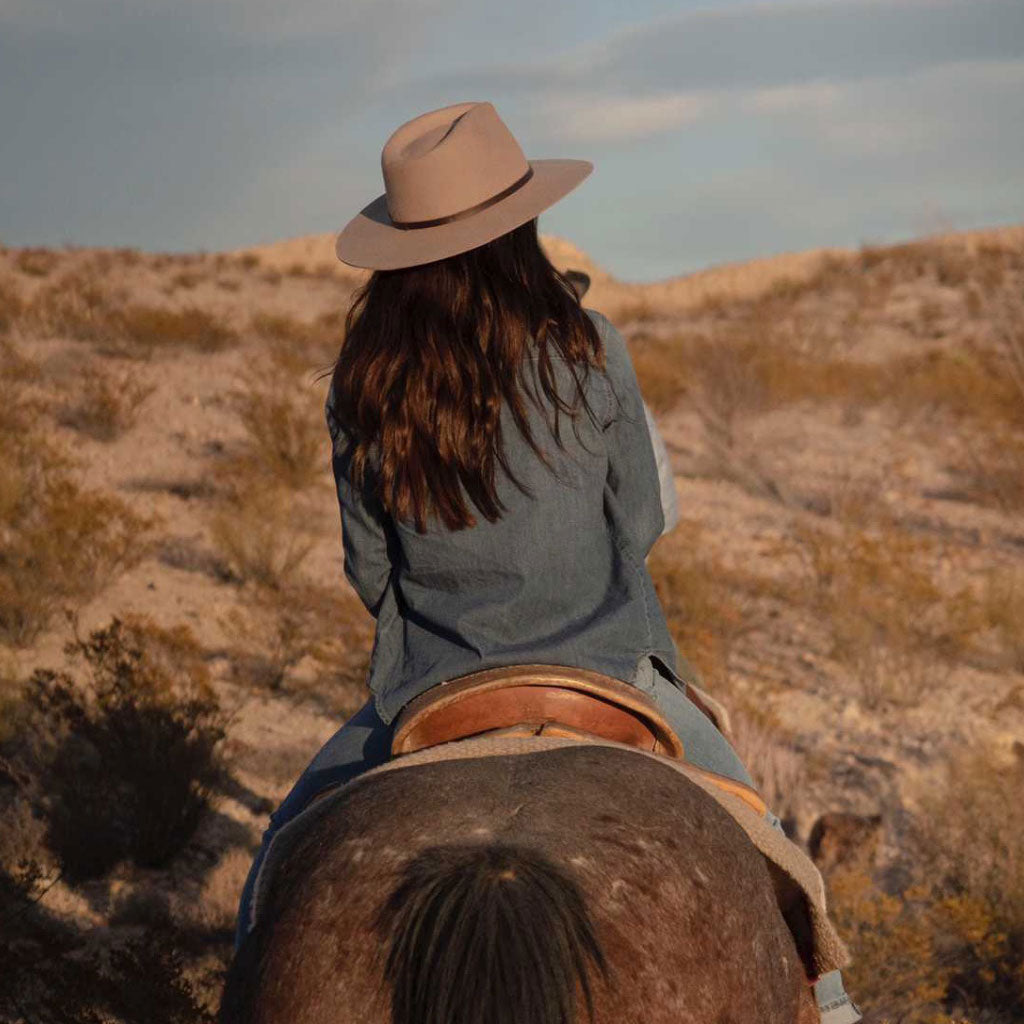 Woman riding a horse in stiff raw edge western outback wool hat with wide flat brim in Brown color with dark leather band