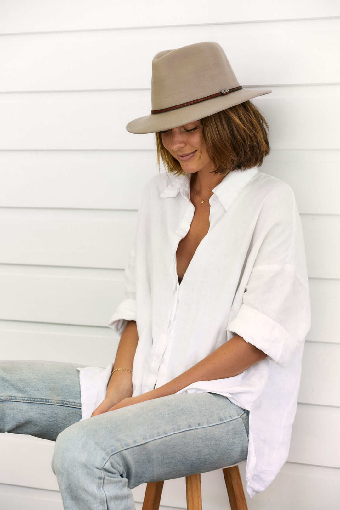 Woman sitting outside outside in Putty wool outback hat with thin tooled leather hat band and Conner emblem