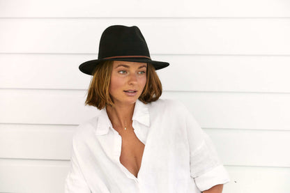 Woman sitting outside in Black wool outback hat with thin tooled leather hat band 